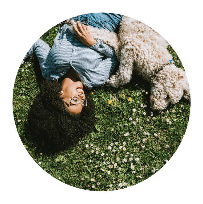 Woman lying in grass with her curly haired dog.